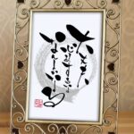 アンティーク調のゴールドのフォトフレームに収められた、縦書きの作品。中央背景には薄い墨色の円(円相)が描かれ、その上に重なるようにして『大丈夫、心配するな、なんとかなる』という言葉の筆文字。躍動感のある力強い筆致で三行にわたって書かれ、左下には「みどり」の赤い落款(印)が押されています。