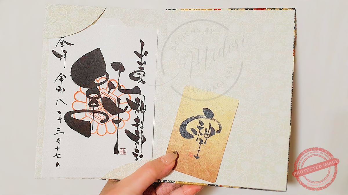 御朱印帳に納められた「絆」の筆文字御朱印と、カードタイプの「そしじ」御守